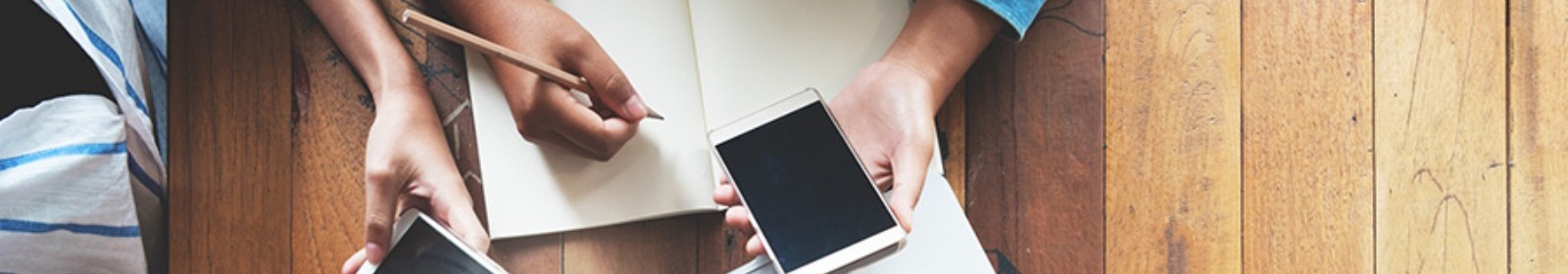 Two people are looking at their mobile phones with a writing pad