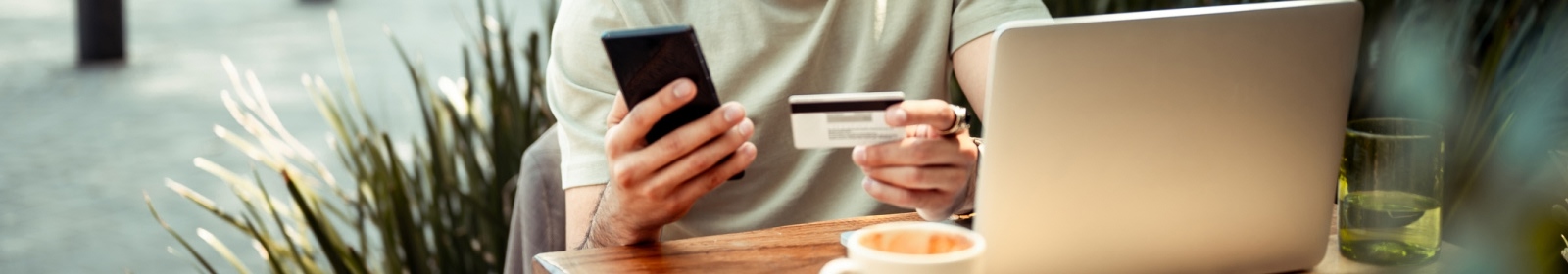 a person holding a mobile phone, and a credit/debit card at a coffee shop